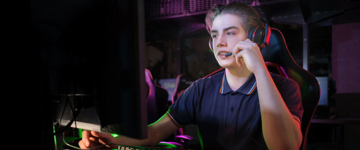 A gamer wearing a headset in front of a monitor. Blue light emission is 76% for conventional monitors, while it is 46% for OLED, emphasizing that OLED display emits up to 39% less harmful blue light.