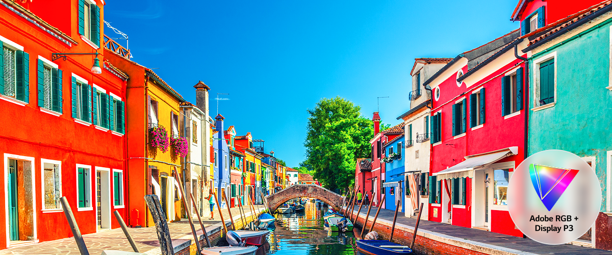 A side-by-side comparison of 'Conventional IPS' on the left and 'Neo:LED' on the right. Both screens display an image of Burano Island, Italy, with the Neo:LED display showing more vivid and rich colors. The conventional IPS features an icon in the lower-left corner indicating support for the Adobe RGB color gamut, whereas the Neo:LED has an icon in the lower-right corner that signifies support for both Adobe RGB and Display P3 color gamuts.